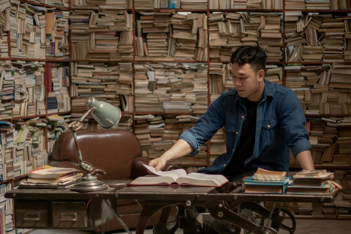 Homem estudando finanças, cercado por livros, simbolizando que o conhecimento é a melhor bússola para autonomia financeira e investimentos.